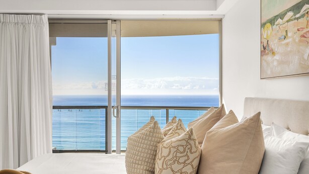 Un dormitorio con un amplio ventanal corredizo que da a un balcón con vistas al océano.