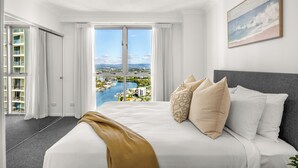 Habitación de hotel con una cama grande, vistas a un puerto deportivo y un balcón con vista panorámica de la ciudad.