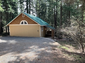Une cabane en bois avec un toit vert, une véranda et une allée gravillonnée.