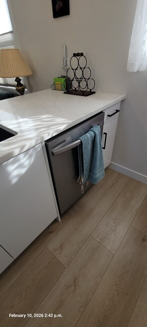 A kitchen with a white countertop, a dishwasher, and a towel hanging on the door.