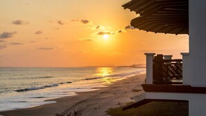 A beach view with a sunset, a wooden fence, and a white building with a roof. - 3-bedroom Condo with AC, WiFi, Ocean Views, Tennis court & Gym in Vivo resorts (Bajos de Chila)