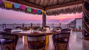 A round dining table with chairs, a thatched roof, and colorful flags. - 3-bedroom Condo with AC, WiFi, Ocean Views, Tennis court & Gym in Vivo resorts (Bajos de Chila)