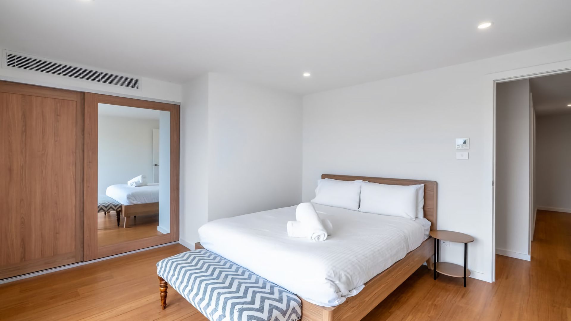 A bedroom with a wooden bed, a bench, a bedside table, and a mirror.