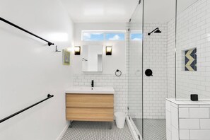 A modern bathroom with a white vanity, a glass shower enclosure, and a small window above the mirror. - Stunning Luxurious Home, near Beverly Hills & DTLA (Los Angeles)