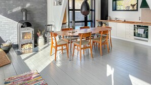 A modern kitchen with a wood-burning stove, a dining table with chairs, and a large window. - Beautiful home in Vejby with sauna (Vejby)