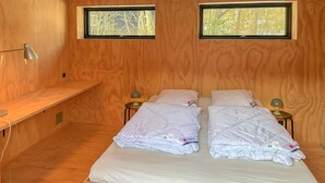 A wooden room with two beds, each with a pillow and a small table with a lamp. There are two windows with a view of trees. - Beautiful home in Vejby with sauna (Vejby)