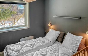 Makuuhuoneessa on sänky, yöpöytä, seinälle kiinnitetty hylly ja ikkuna, josta avautuu näkymä puihin ja rakennukseen.