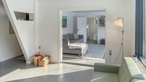 A modern living room with a grey sofa, a green armchair, and a large window. There is a staircase leading to an upper level, and a door to a bedroom. - Beautiful home in Vejby with sauna (Vejby)