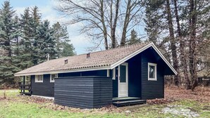 Eine kleine, dunkel gefärbte Holzhütte mit einem geneigten Dach, einer Haustür und einer kleinen Veranda.