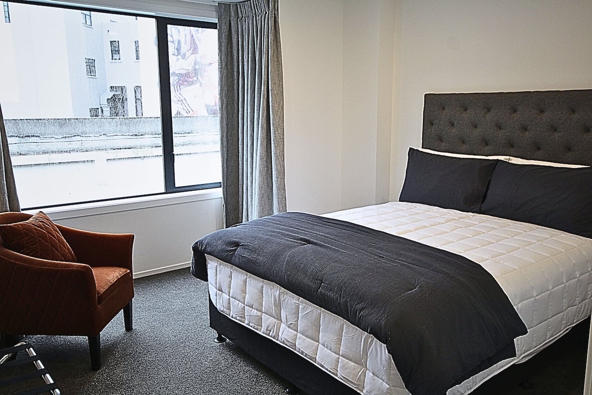 Un dormitorio con una cama grande, una silla y un ventanal con cortinas.