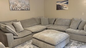 A sectional sofa with multiple cushions, a matching ottoman, and a patterned rug. - Resort Pool, Hot Tub, Firepit & Cornhole (Branson)