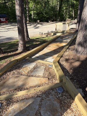 A wooden pathway with stone slabs and gravel, surrounded by trees. - Resort Pool, Hot Tub, Firepit & Cornhole (Branson)