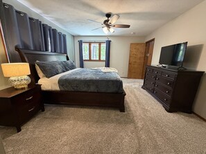 A bedroom with a bed, a dresser, a television, a ceiling fan, and a window with curtains. - Resort Pool, Hot Tub, Firepit & Cornhole (Branson)