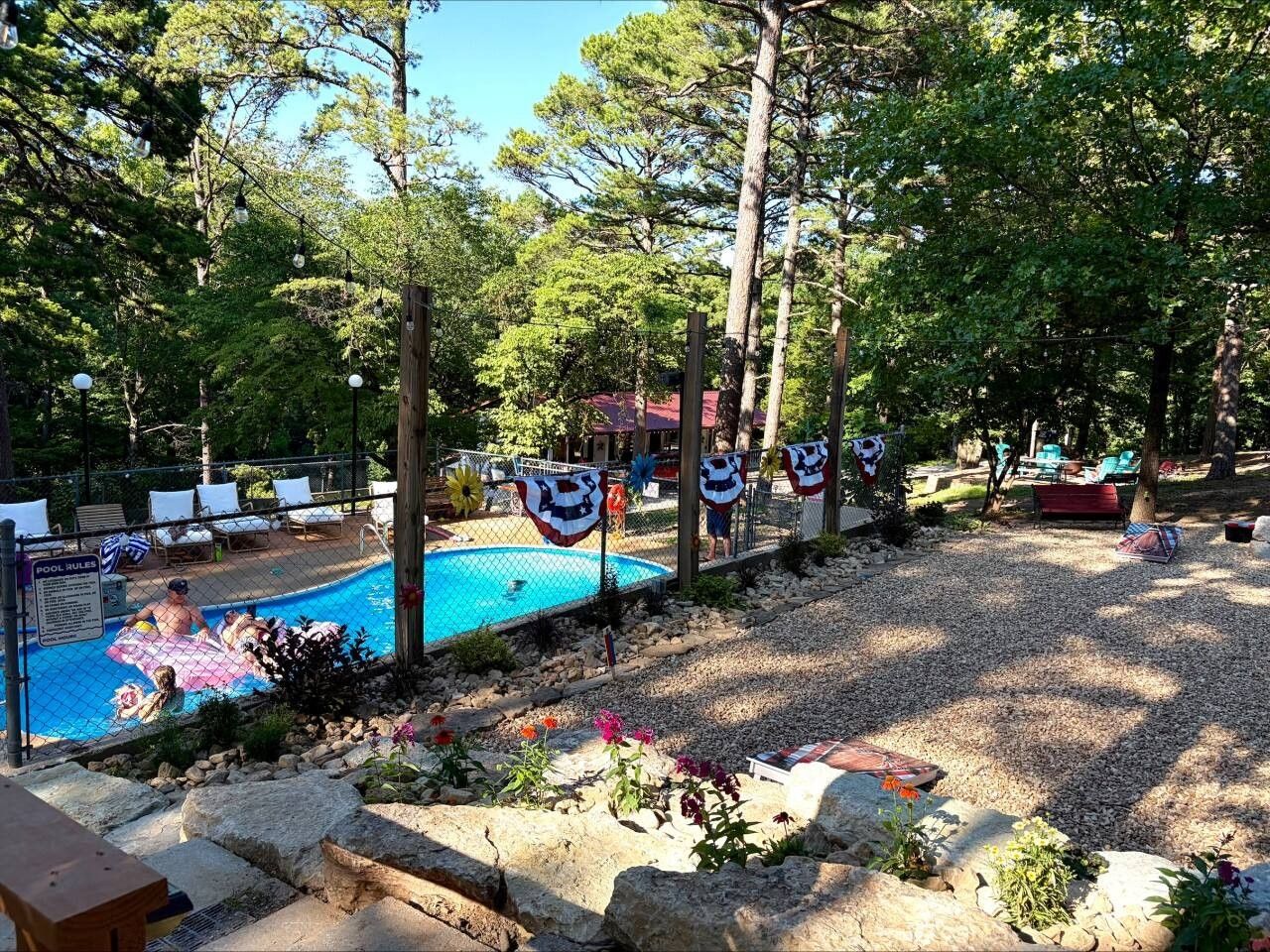 Une piscine entourée d’une clôture, avec des chaises longues et un mât sur lequel sont hissés des drapeaux.