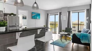 Een modern appartement met keuken, eethoek en woonkamer. Het heeft een groot raam, een balkon en uitzicht op de stad.