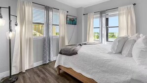 Een slaapkamer met een bed, gordijnen, een vloerlamp en uitzicht op de omgeving.