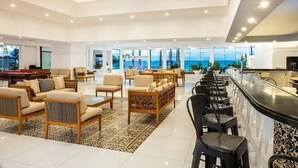 Un hall d’hôtel spacieux doté d’une table de billard, de sièges confortables, d’un bar et de grandes fenêtres offrant une vue sur l’océan.
