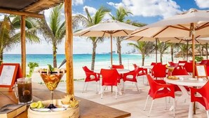 Un restaurant situé en bord de mer, avec des chaises rouges et des parasols blancs, offrant une vue sur l’océan.