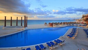Un espace piscine doté de chaises longues et de parasols, avec vue sur l’océan.