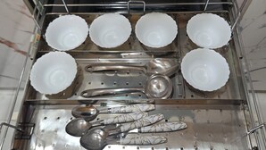 Eine Küchenschublade mit verschiedenen Küchenutensilien und Geschirr, darunter Schüsseln, Löffel und ein Sieb.
