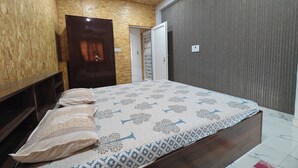 Ein Schlafzimmer mit Holzboden, einem Bett mit gemusterten Betttextilien, einem Kleiderschrank und einer Tür zu einem weiteren Raum.