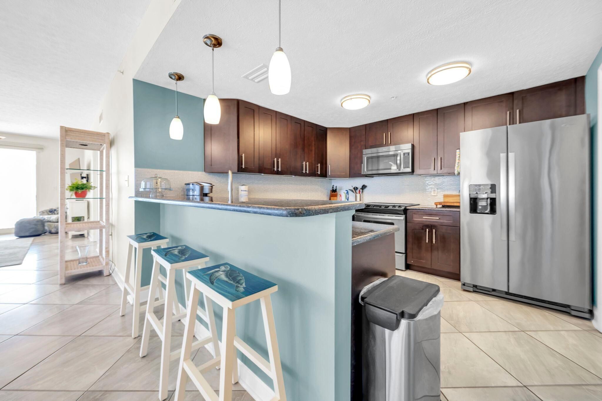 A modern kitchen with dark wooden cabinets, a stainless steel refrigerator, and a central island with bar stools.