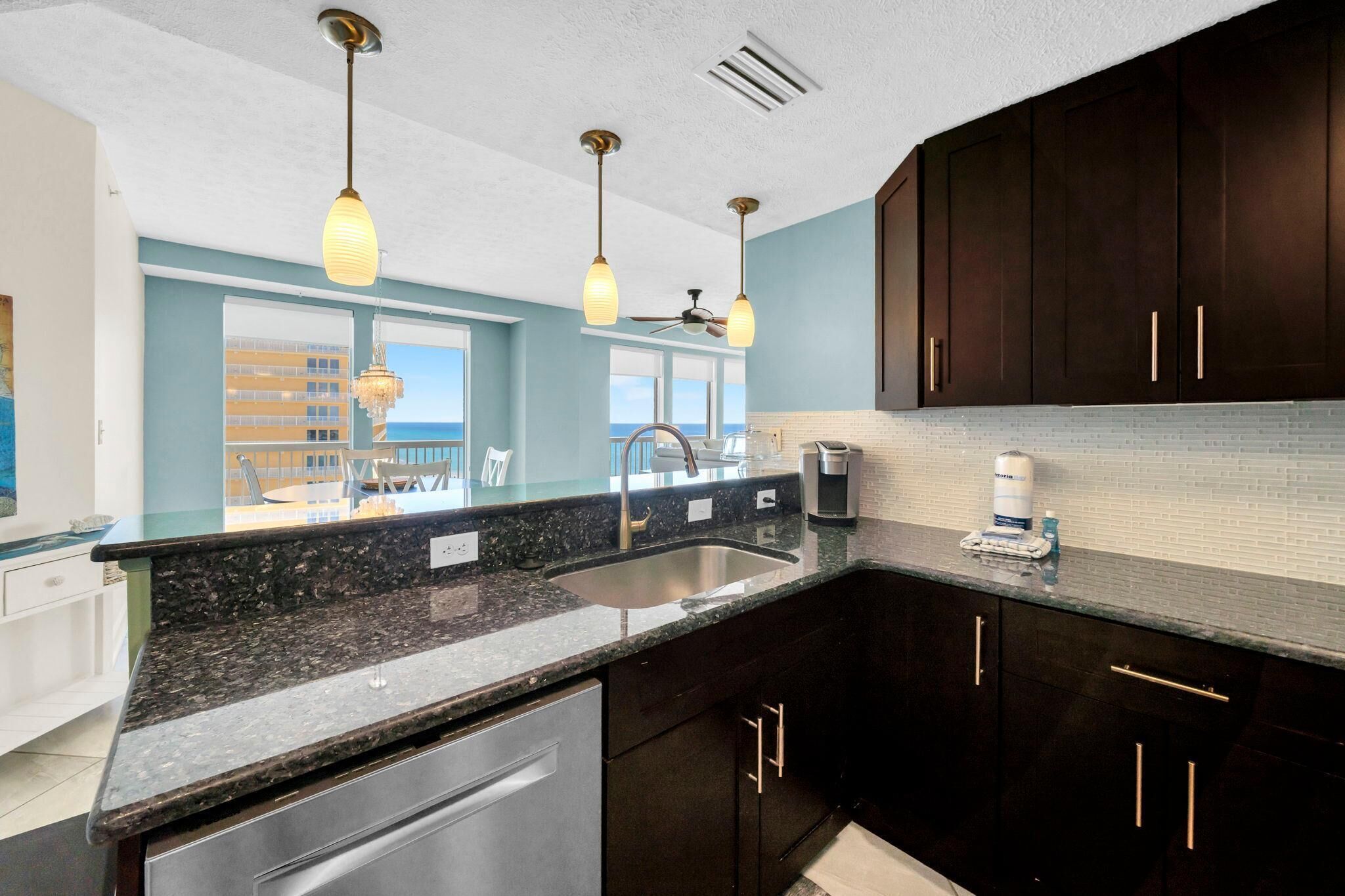 A modern kitchen with dark cabinets, granite countertops, and pendant lighting.