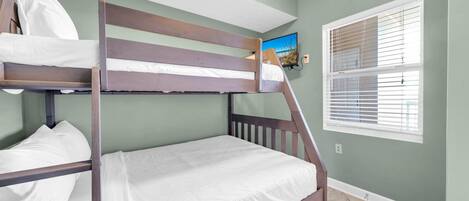 Una cama litera con ropa de cama blanca en una habitación con paredes verdes y una ventana con persianas.