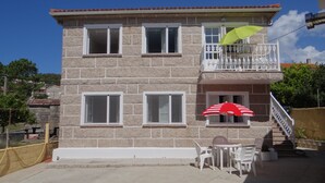 Un edificio de piedra de dos pisos con un balcón, una mesa con sillas y un paraguas a rayas rojas y blancas.