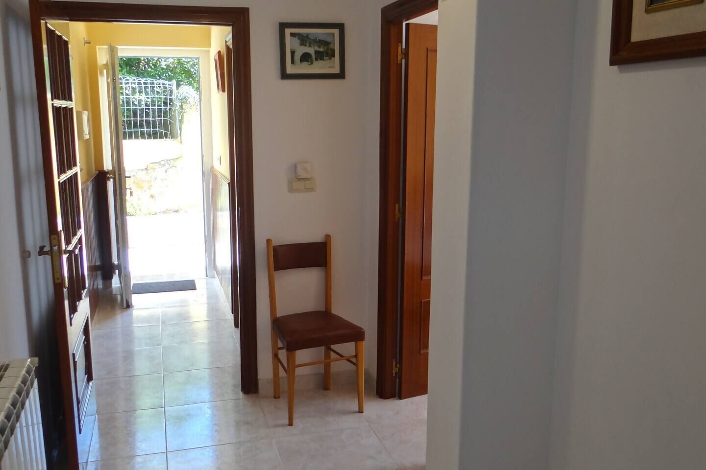 Un couloir avec une chaise en bois, une porte et un tableau encadré accroché au mur.