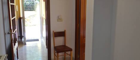 Un couloir avec une chaise en bois, une porte et un tableau encadré accroché au mur.