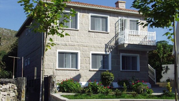 Un edificio de piedra de dos pisos con un balcón, ventanas y un muro de piedra frontal.