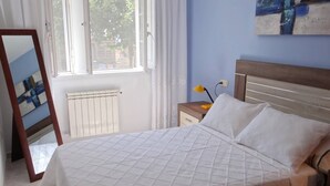 Un dormitorio con cama, mesita de noche, espejo y ventana con cortinas.
