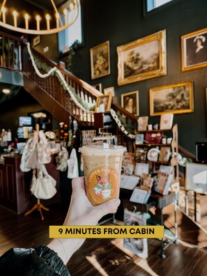 A hand holding a cup with a fox design, inside a cafe with a staircase and framed pictures on the wall. - Blue Ridge Wellness Cabin | Peak Retreat (Blue Ridge)