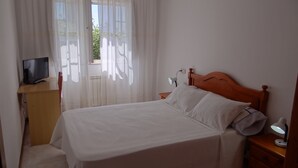 A neatly made bed with white linens, a wooden headboard, and a bedside lamp. There is a small wooden nightstand with a lamp, and a television on a wooden desk. - Ignacio C at the beach in Lariño (Lariño)