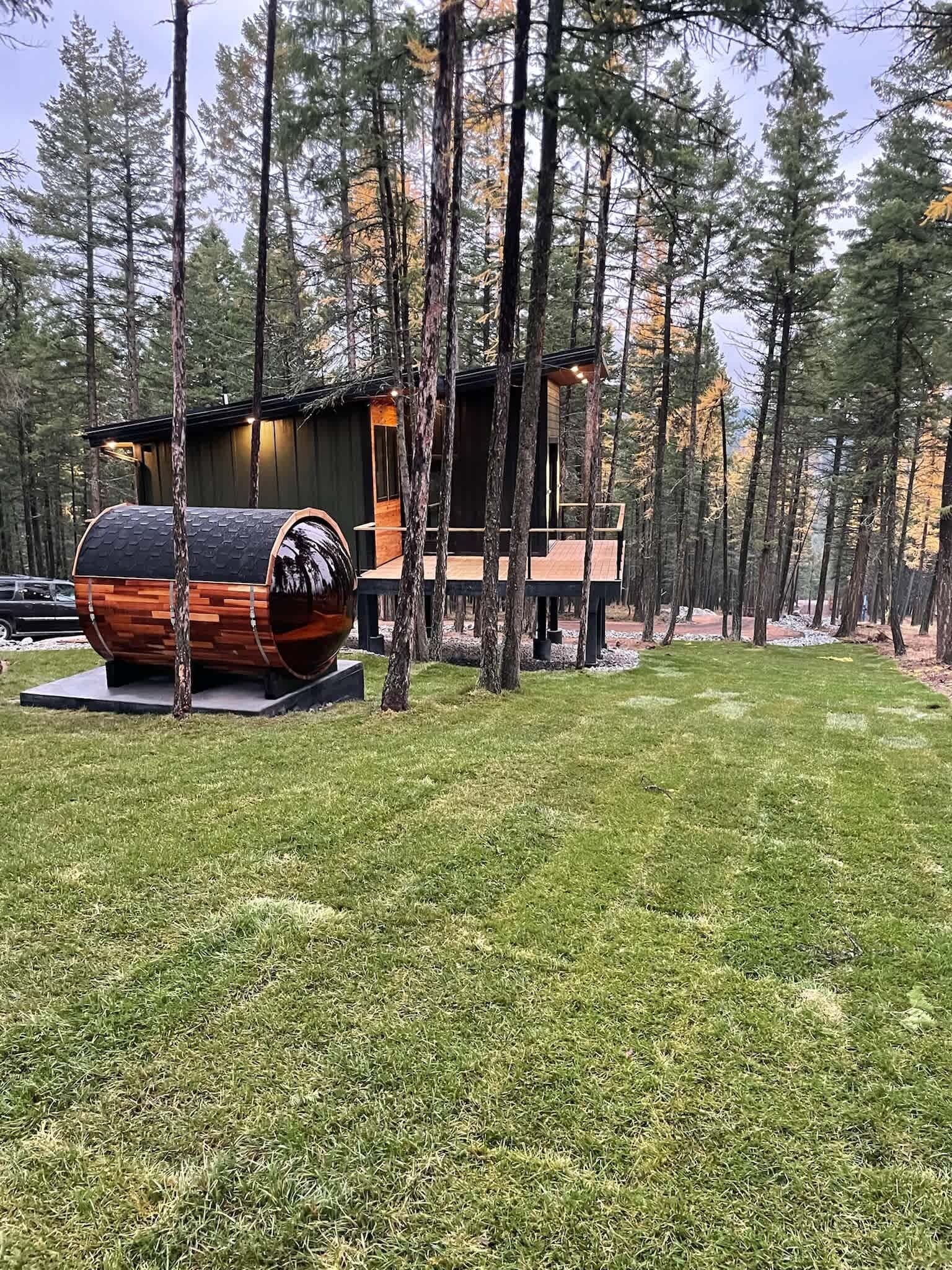 A cabin with a unique barrel-shaped structure in the foreground, surrounded by a forest.