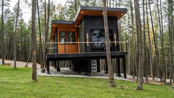 Une cabane moderne dotée d’une terrasse en bois, entourée d’une forêt.