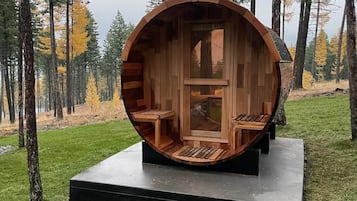 Une structure en bois qui ressemble à un tonneau, avec un banc à l’intérieur, installée sur une plateforme au cœur d’une forêt.