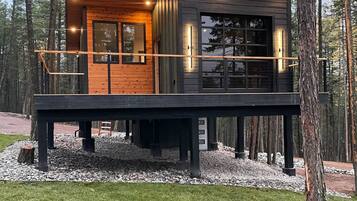 Une cabane moderne dotée d’une terrasse en bois, de grandes fenêtres et de fondations en pierre.