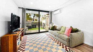Un soggiorno con TV a schermo piatto, un divano con cuscini, un tappeto decorato e una porta vetrata scorrevole che dà su una zona esterna con biciclette.