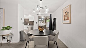 A modern dining area with a round table, grey chairs, a vase with flowers, and a unique chandelier.
