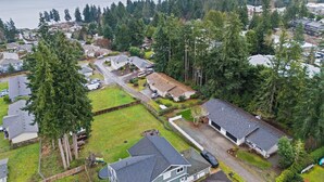 An aerial view of a residential area with houses, a large body of water, and a forested hill in the background.