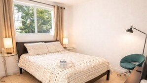 Een keurig opgemaakt slaapkamer met een bed, nachtlampjes, een bureau en een stoel.
