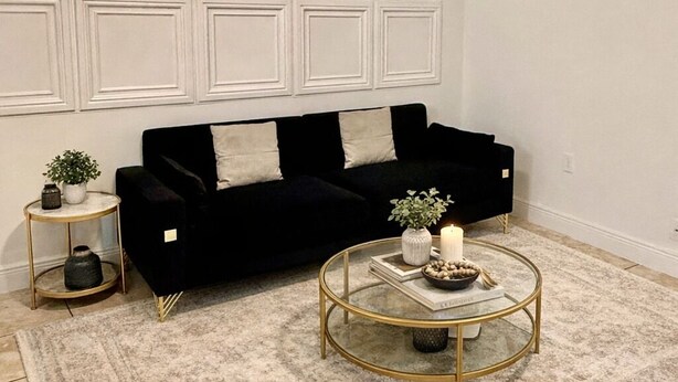 Een woonkamer met een zwarte bank, een ronde salontafel, een bijzettafeltje en een vloerkleed met dessin.