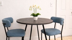 Een ronde tafel met een witte vaas met bloemen, twee blauwe stoelen en een witte deur op de achtergrond.