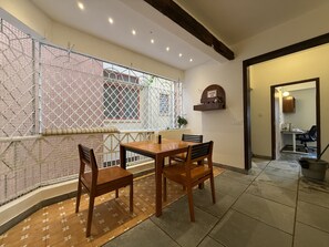 A dining area with a wooden table and chairs, a decorative wall, and a window with a metal screen.