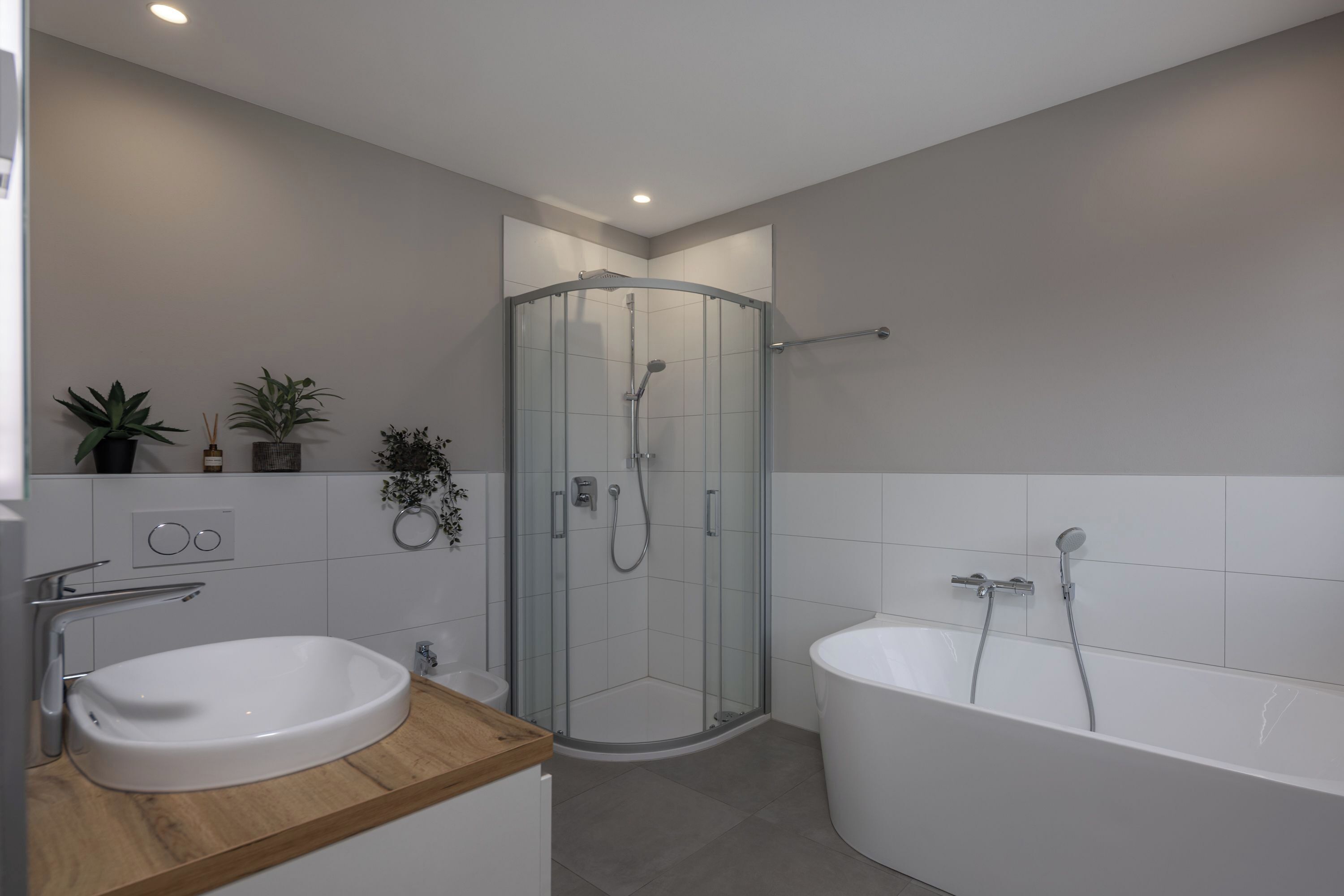Un baño moderno con ducha envuelta en cristal, una bañera independiente y un lavabo con encimera de madera.