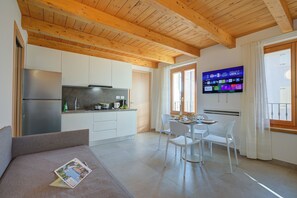 Una cocina moderna con armarios blancos, un refrigerador de acero inoxidable y un comedor con mesa y sillas blancas.