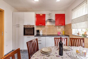 A compact kitchen with white cabinets, a red range hood, and a dining area with a table set for two. - Pool Apt 2 - Novi Vinodolski (Sea View), Novi Vinodolski, Croatia (Novi Vinodolski)