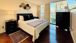 Una camera da letto con un letto, comodini, una cassettiera e un'ampia finestra vista città.